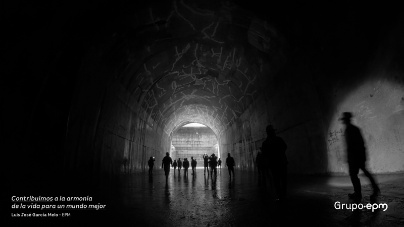 Foto tomada por Luis García en balnco y negro, de un túnel en una central, al fondo la luz refleja las sombras de los trabajadores