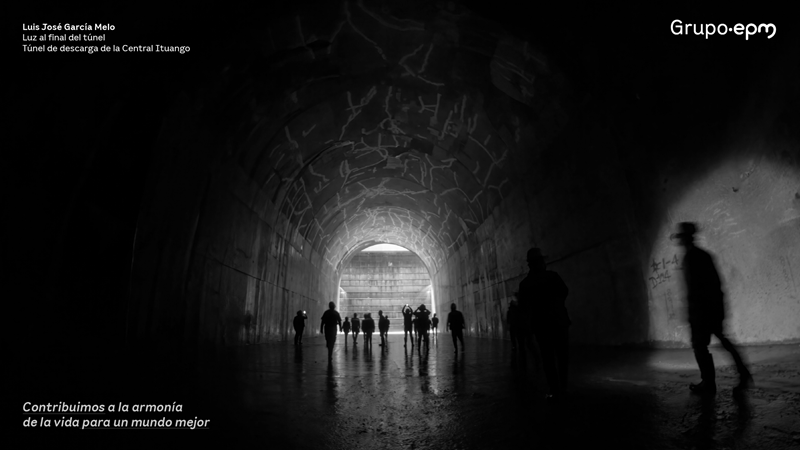 Foto tomada por Luis García en balnco y negro, de un túnel en una central, al fondo la luz refleja las sombras de los trabajadores