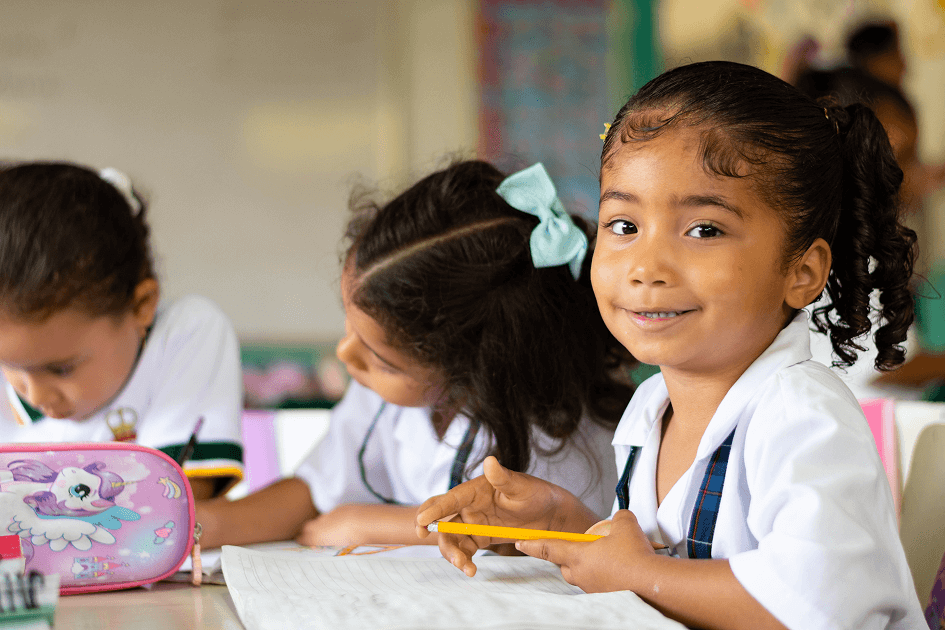 Niñas en uniforme escolar sonriendo mientras escriben en sus cuadernos en clase