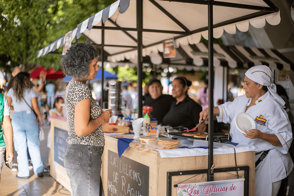 Mujer atiende un puesto de comida en una feria comunitaria al aire libre