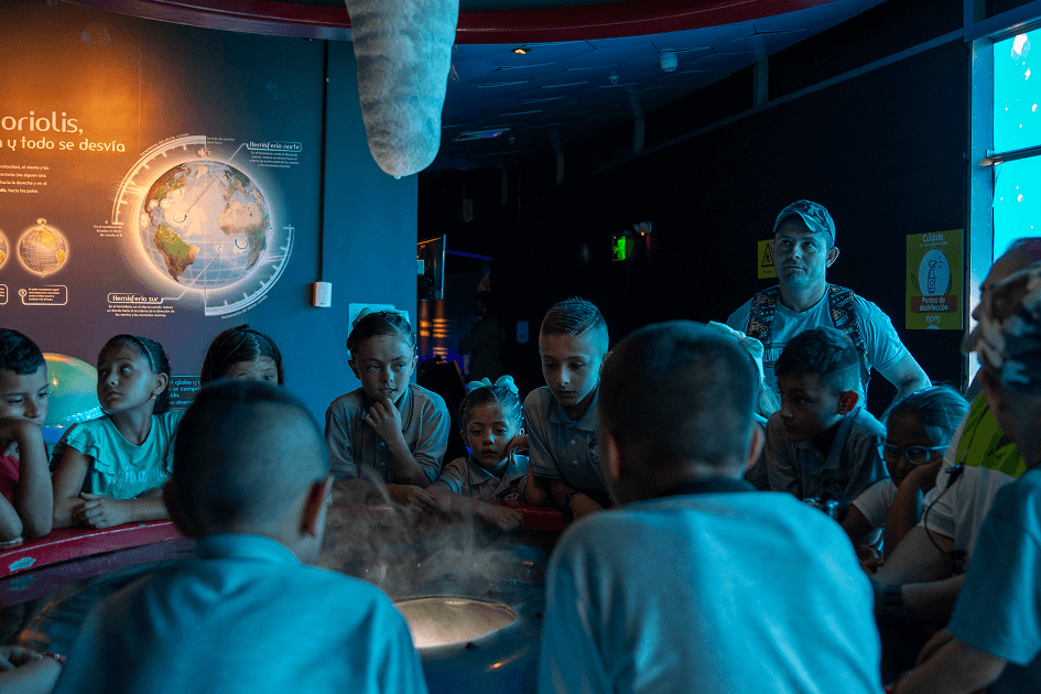 Grupo de niños observando una demostración interactiva sobre fenómenos del agua
