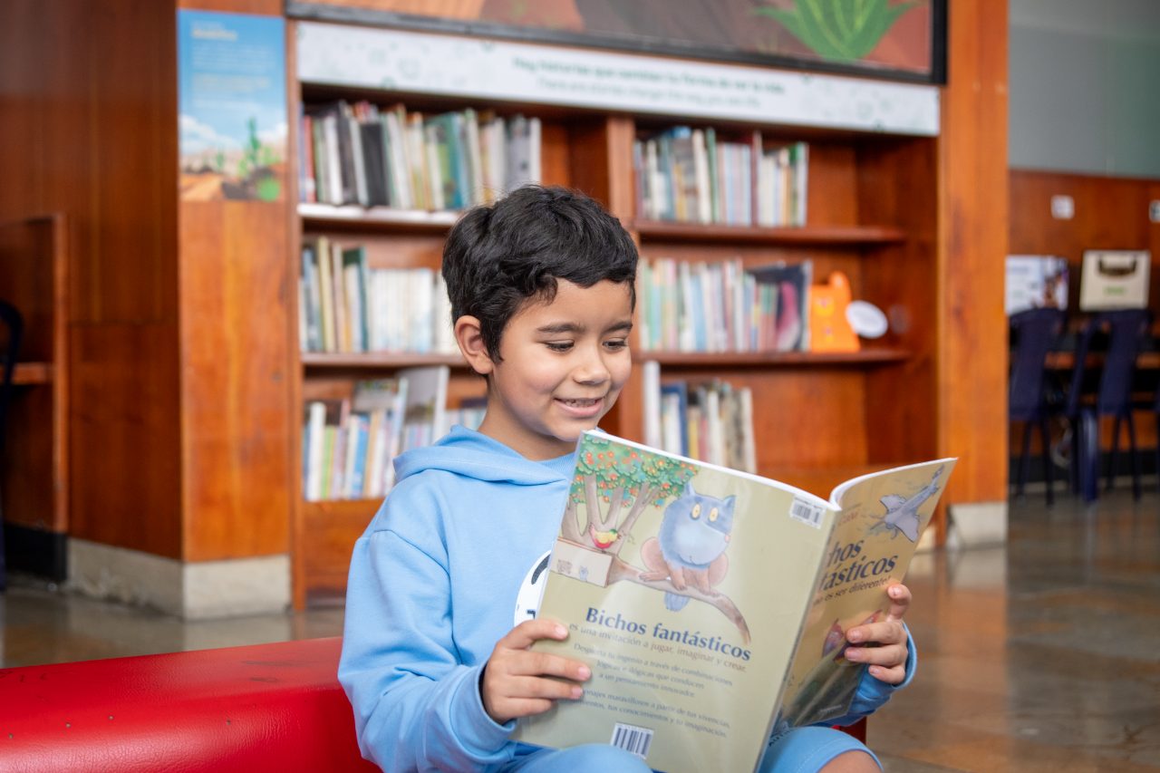 Niño sonriendo mientras lee un libro en la Biblioteca EPM