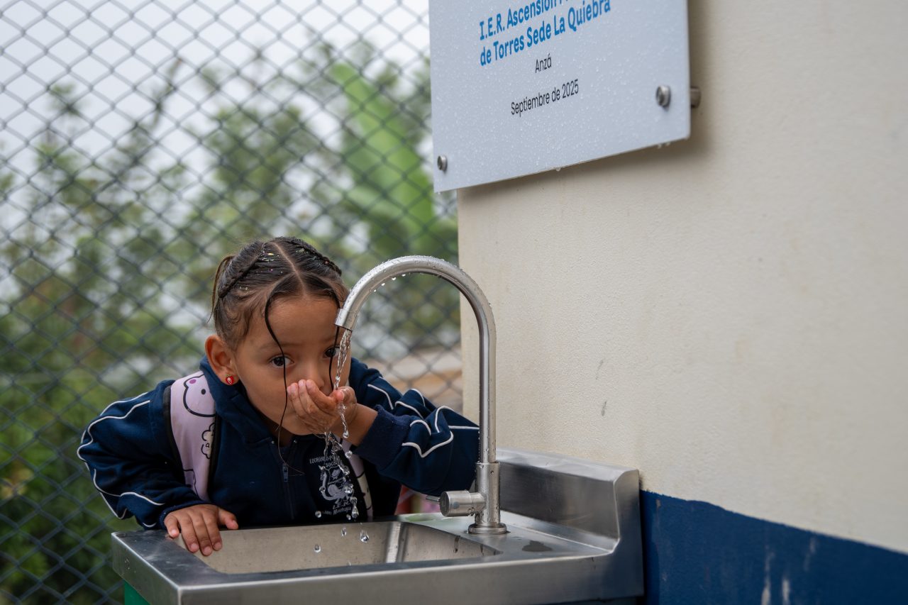 Niña pequeña bebiendo agua de un grifo en una escuela
