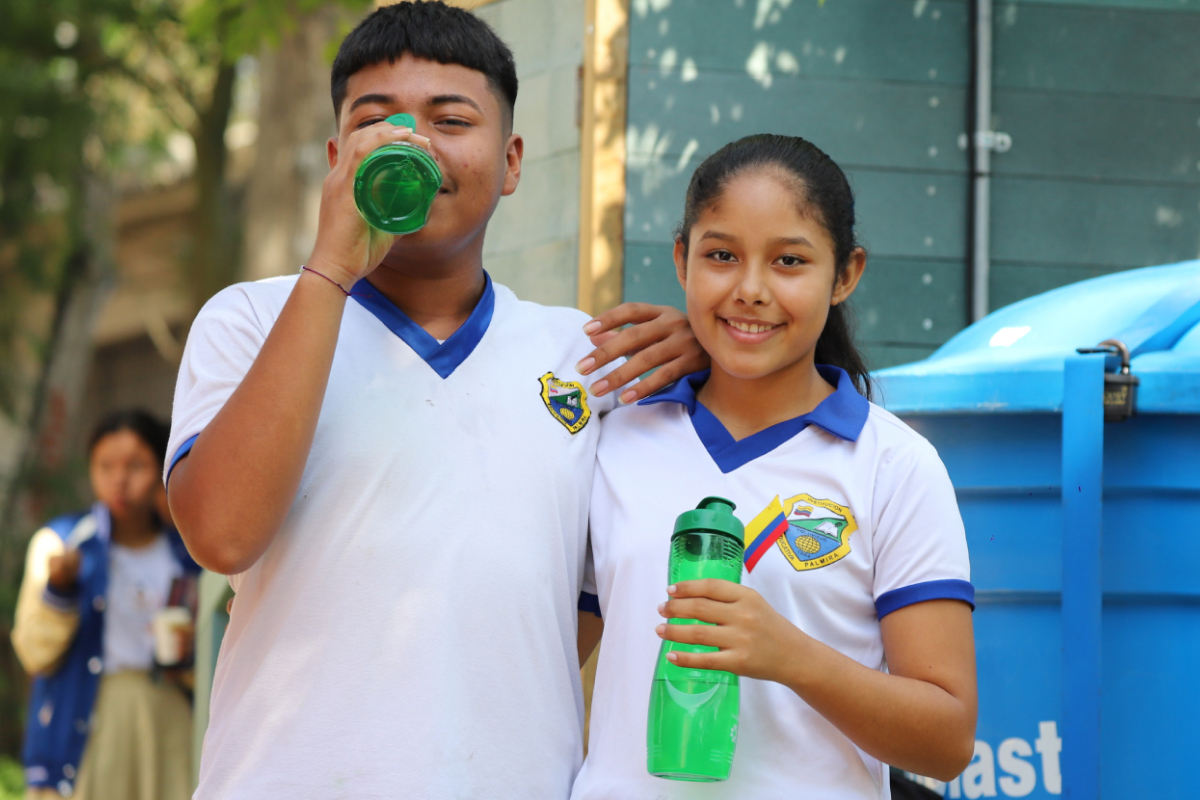 Dos estudiantes con botellas reutilizables bebiendo agua en un entorno escolar.