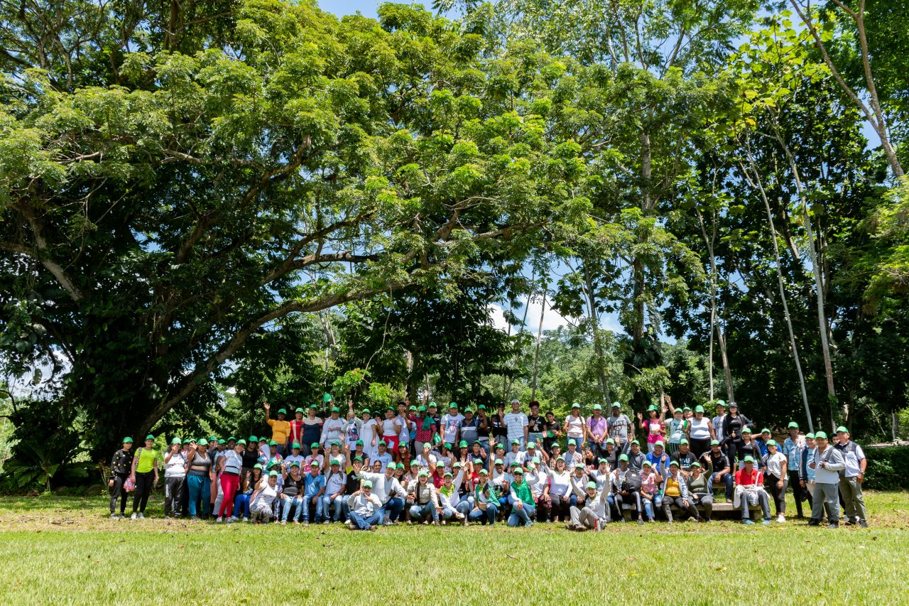 Grupo grande de personas con gorras verdes reunidas en un entorno natural durante una jornada comunitaria.