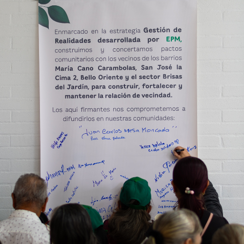 Personas firmando un mural con un compromiso comunitario de la estrategia Realidades desarrollada por EPM, orientado a fortalecer la relación de vecindad.