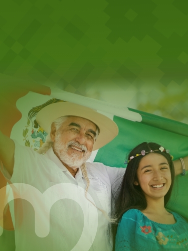 Un señor con cabello largo alzando una bandera de México y una niña con flores en el cabello, 