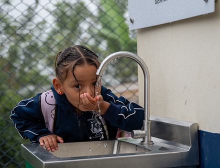 Niña pequeña bebiendo agua de un grifo en una escuela