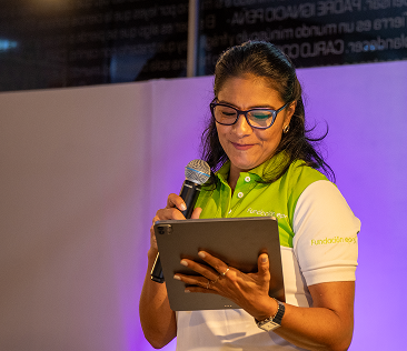 Mujer con camiseta institucional de la Fundación EPM lee desde una tableta mientras habla por un micrófono en un evento.